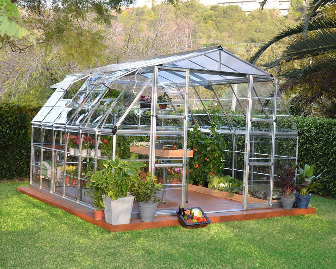 Americana 12x12 greenhouse in a lush garden with plants on wooden base