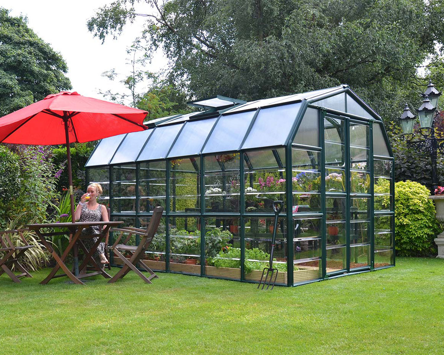 Grand Gardener Greenhouse Kit in a real garden setting with patio furniture