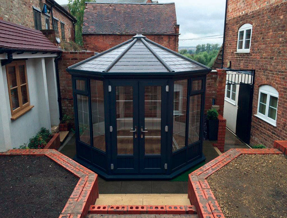 Hexagonal greenhouse with dark roof and transparent walls in a residential area.