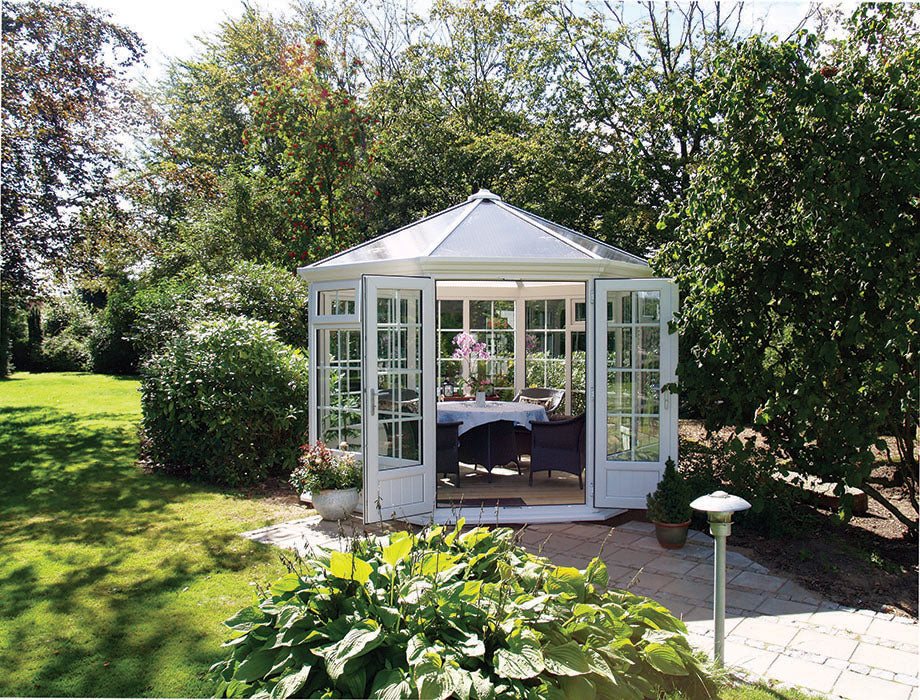 Hexagonal garden shed in a garden setting with greenery and a paved area.